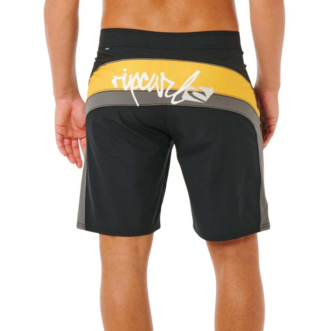 Bañador surf Rip Curl Mirage Archive amarillo y negro, vista trasera con panel cut-and-sew amarillo, logo script Rip Curl blanco y etiqueta Mirage en cinturilla.