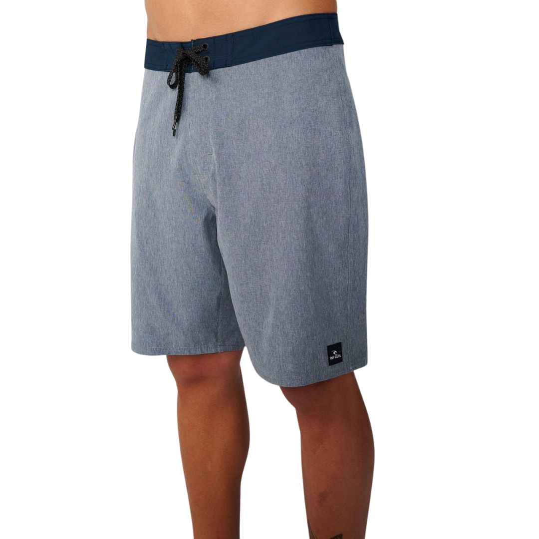 Boardshort azul marino Rip Curl Mirage Core Navy, vista lateral con cinturilla navy contrastada, tejido heather gris y etiqueta Rip Curl en bajo.