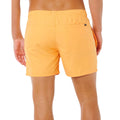 Bañador naranja vivo Rip Curl Offset Volley, vista lateral con mano en bolsillo, cinturilla elástica con cordón gris y etiqueta Rip Curl en bajo.