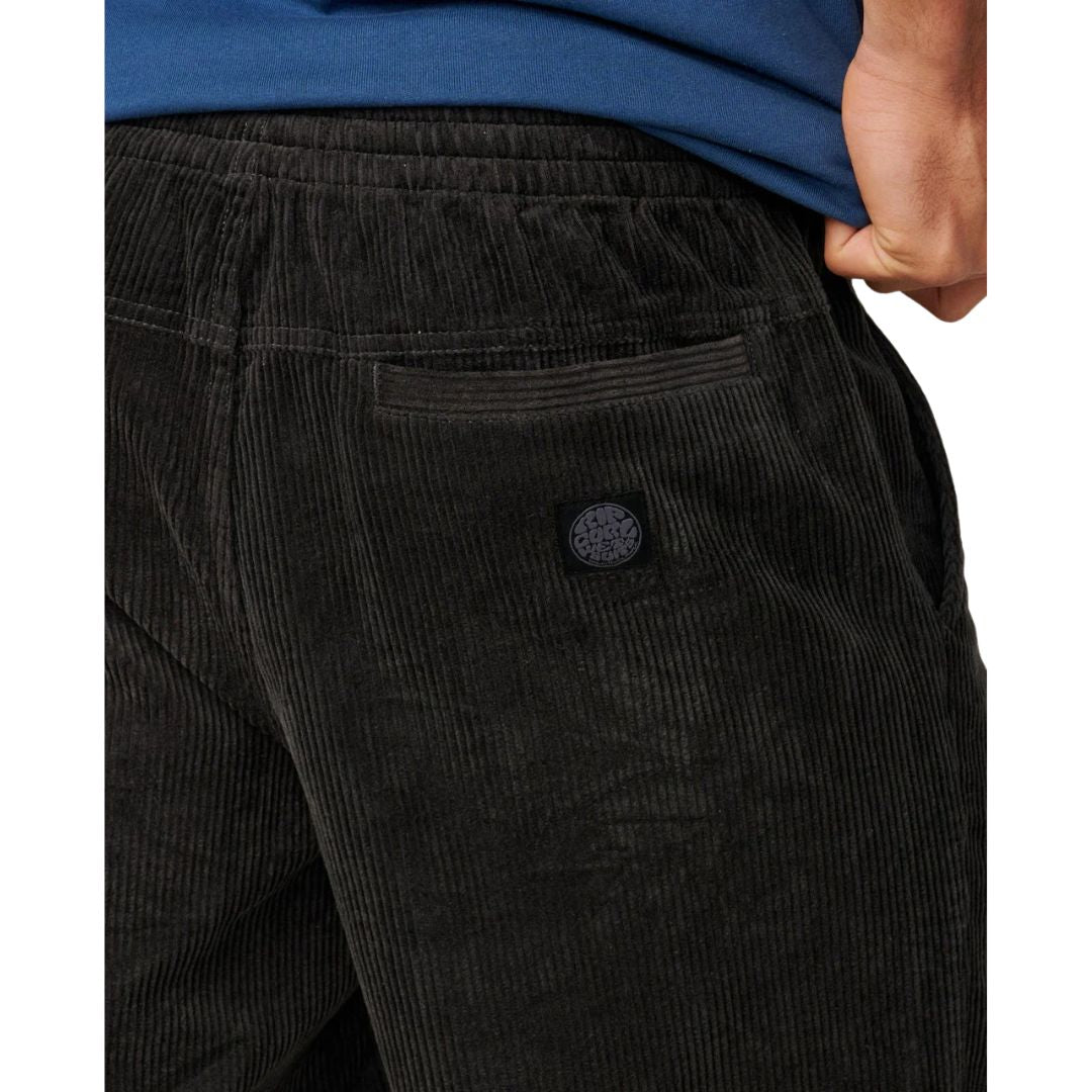 Detalle trasero pantalón corto pana Rip Curl Premium Surf Cord negro, etiqueta tejida circular Rip Curl y bolsillo con solapa en pana acanalada acid wash.