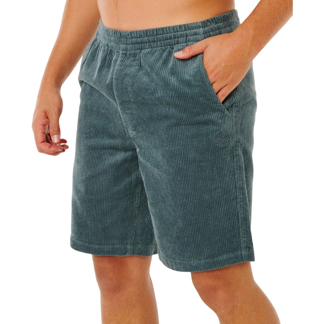 Pantalón corto pana Rip Curl Premium Surf Cord verde pino, vista lateral con mano en bolsillo, logo bordado y efecto desgastado acid wash en pana acanalada.