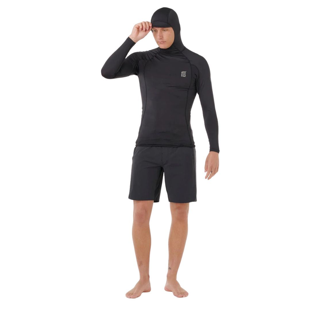 Modelo de cuerpo completo con el conjunto de surf Rip Curl negro, utilizando la capucha técnica ajustada para máxima protección solar UPF.