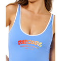 Detalle del logo Surf Puff estampado en bañador Rip Curl azul cielo con texto Surfing Company Since 1969 en degradado rojo naranja y amarillo.