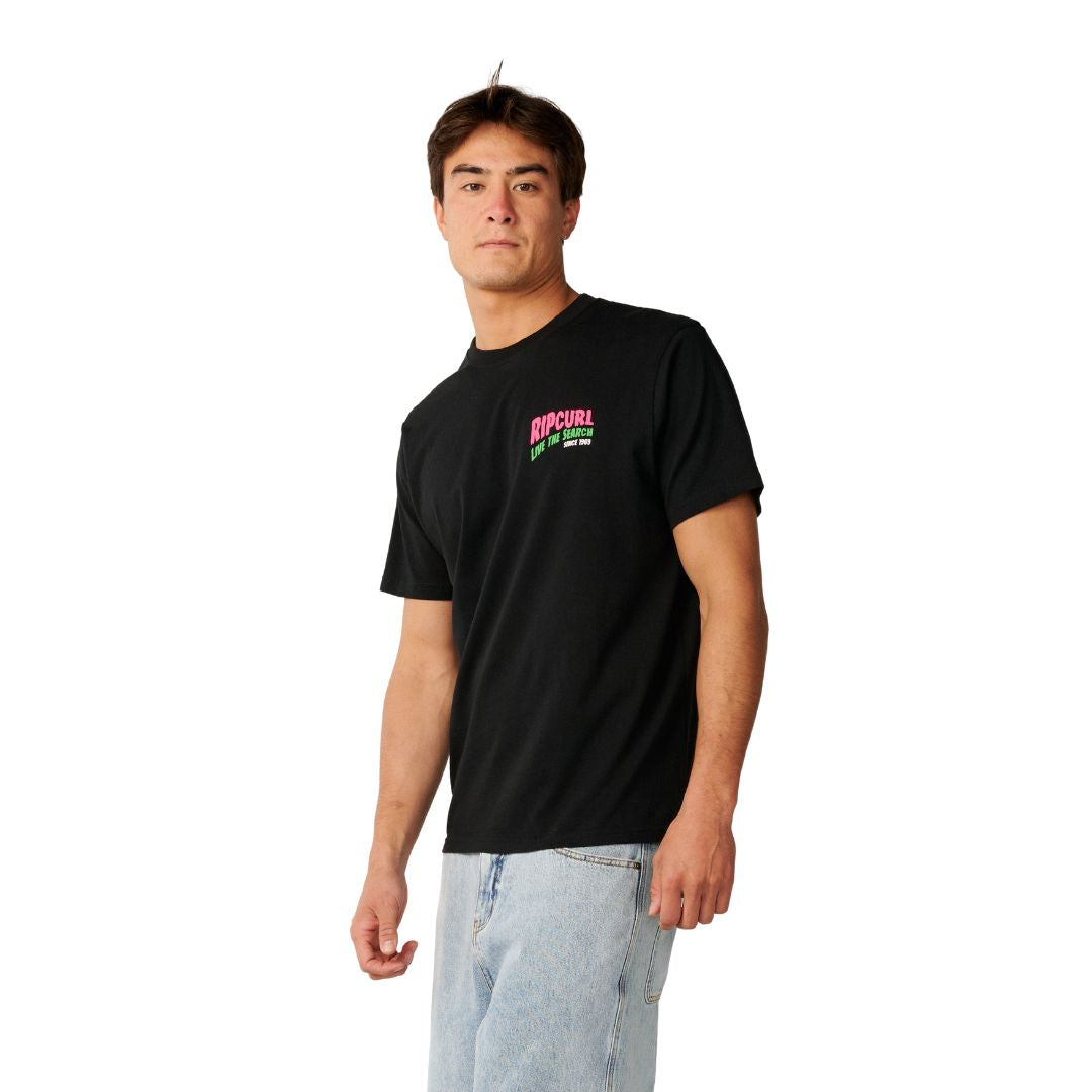 Rip Curl Surf Trip Tee en Black, vista lateral de tres cuartos, mostrando el logo estampado en rosa y verde en el pecho.