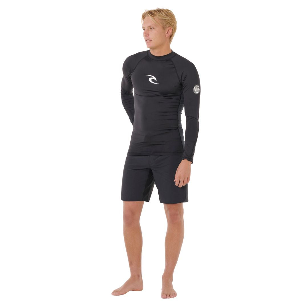 Vista completa del conjunto con licra Rip Curl Waves UPF Perf L/S negra, modelo masculino de pie en postura relajada.