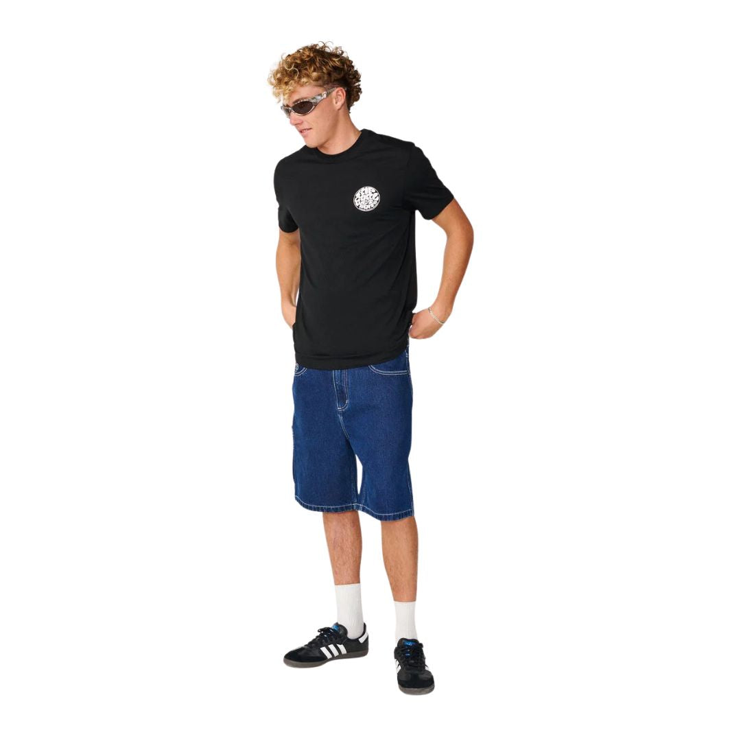Modelo con camiseta Rip Curl Wettie Icon negra combinada con pantalón corto vaquero y zapatillas deportivas.