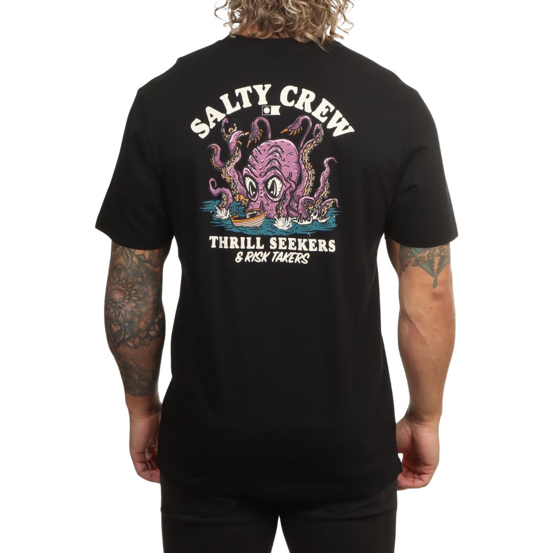 Modelo visto de espaldas con la camiseta Salty Crew Kraken Monster en negro, luciendo el estampado completo del kraken atacando un barco y el texto Thrill Seekers & Risk Takers.