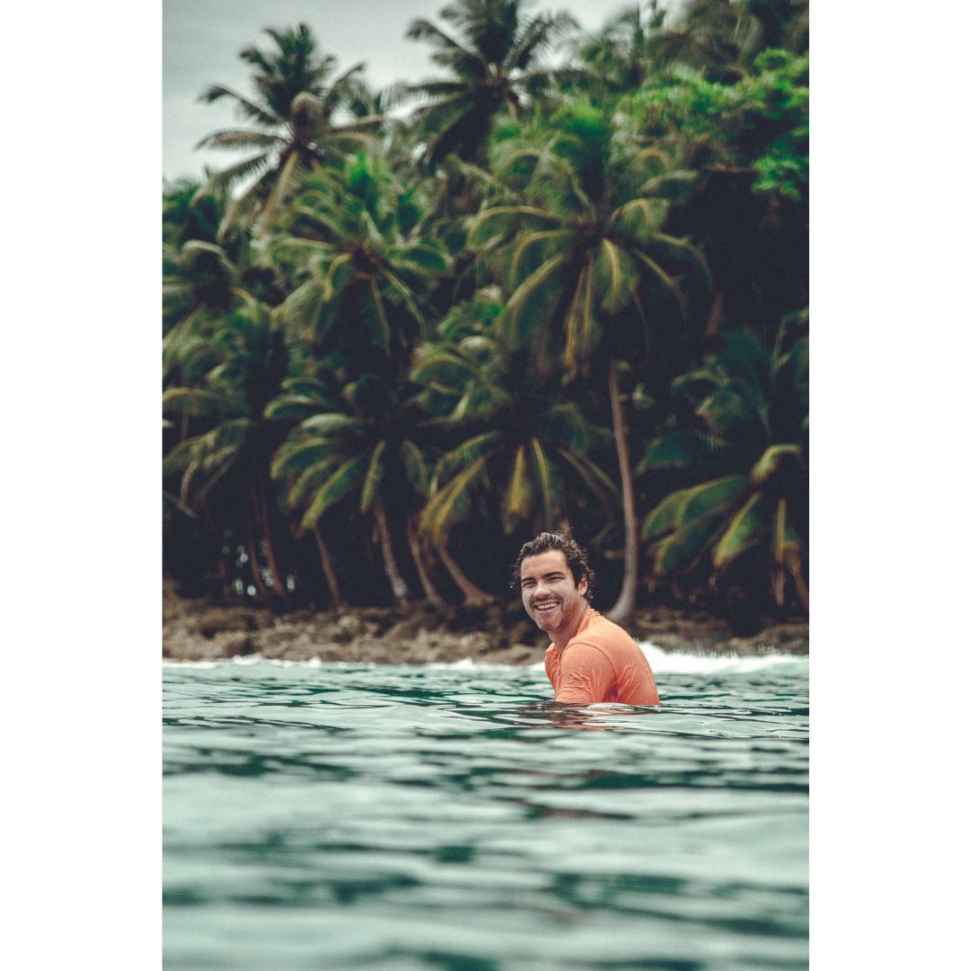 Hombre en el mar con palmeras de fondo usando protector solar resistente al agua Seventy One Percent SPF50+ surf.