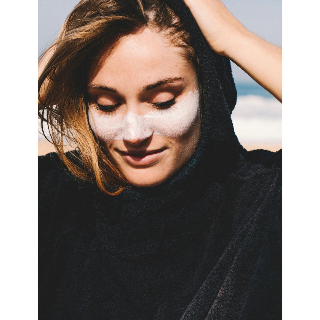 Mujer aplicando protector solar blanco en stick en rostro en playa Seventy One Percent SPF50+ resistente al agua.