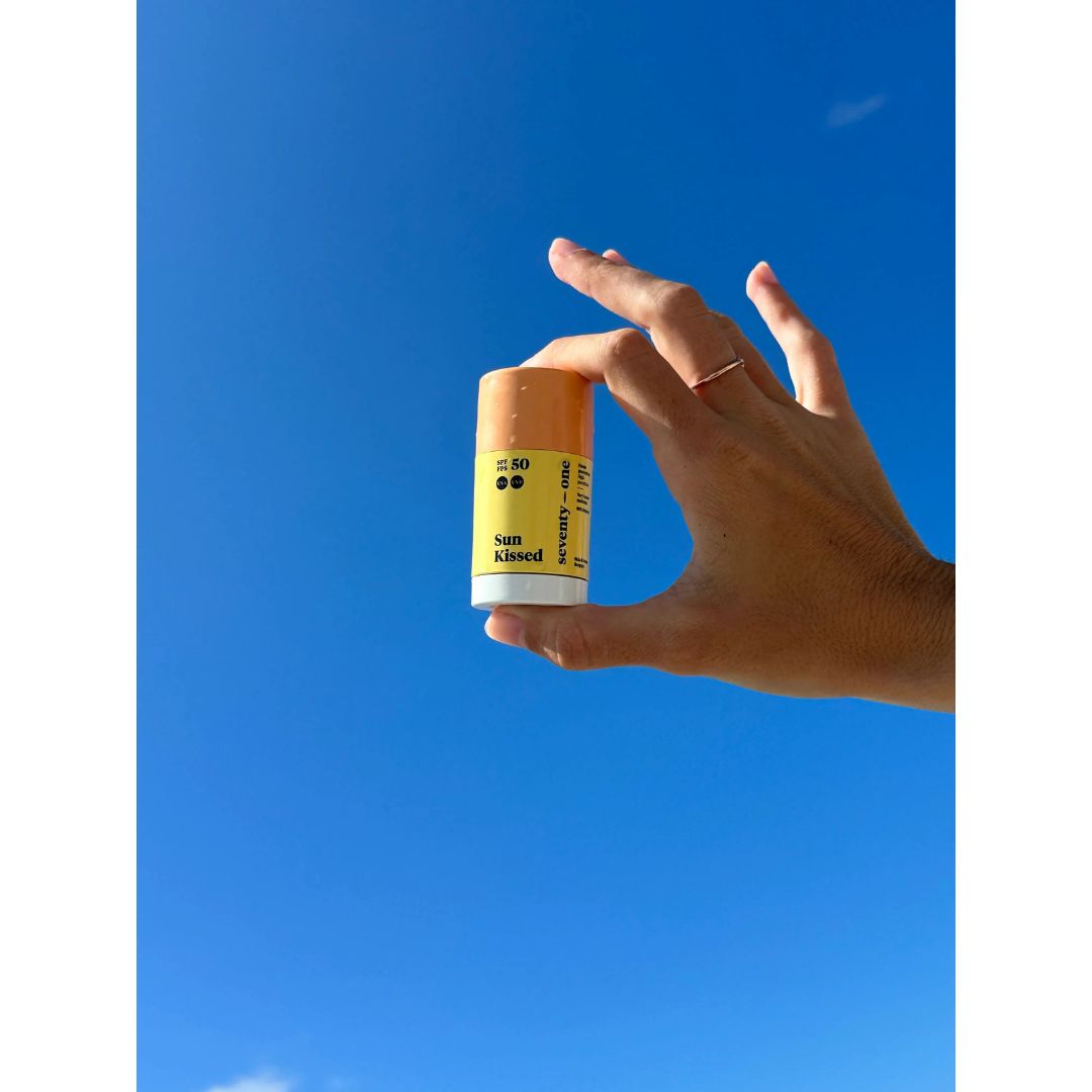 Mano sosteniendo protector solar stick SPF50 invisible Seventy One Percent fondo cielo azul formato portátil.