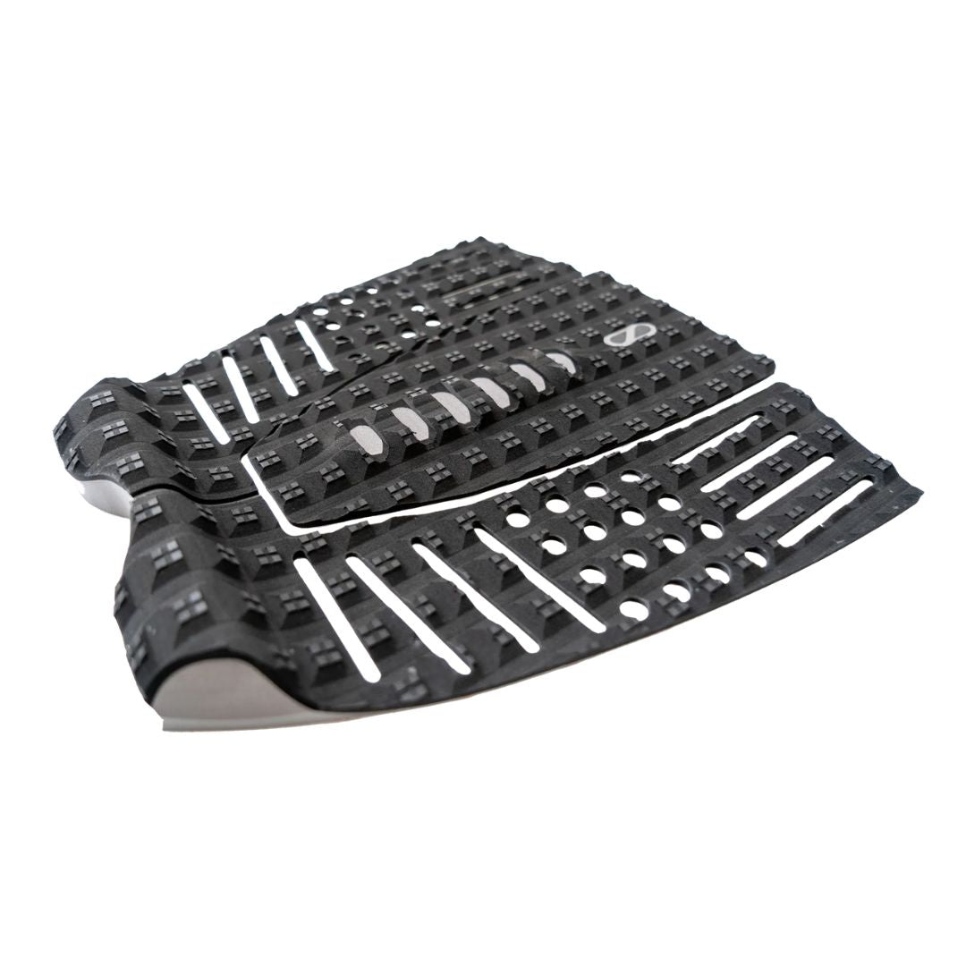 Grip de surf trasero Slater Designs 3 piezas en negro y gris, vista en perspectiva mostrando el arco central con recortes, textura cuadrada BLOOM y kick tail elevado con adhesivo 3M visible.