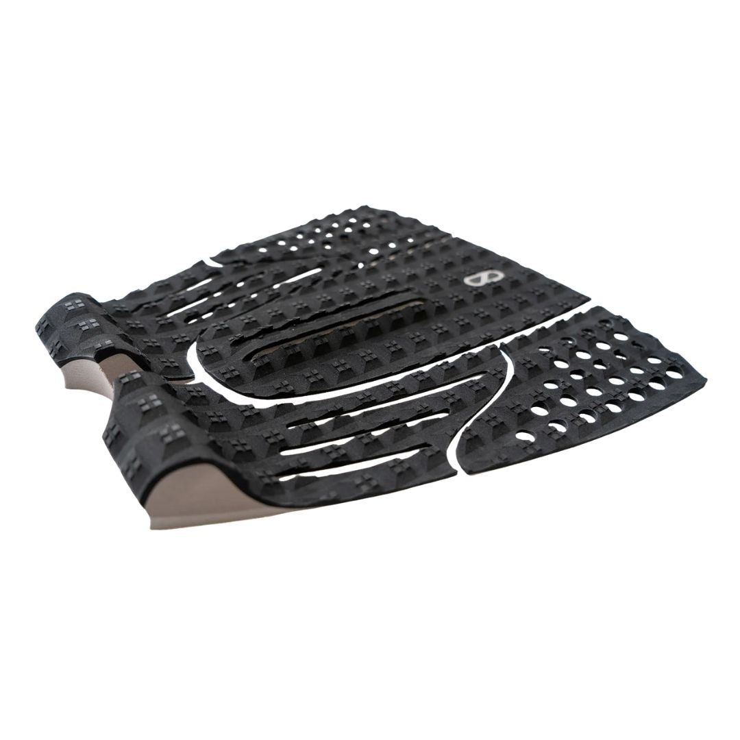 Grip de surf trasero Slater Designs 5 Piece Action Pad negro y gris en perspectiva, mostrando el arco bajo con ranuras paralelas, kick tail con corte en V, textura de diamante BLOOM y adhesivo 3M gris.