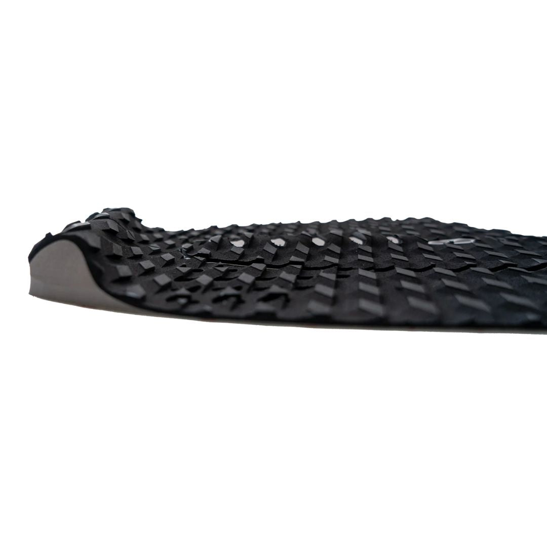 Detalle lateral del grip de surf trasero Slater Designs 5 piezas negro y gris, vista de perfil que muestra la altura del kick tail, textura de diamante BLOOM y el adhesivo 3M gris en la base.