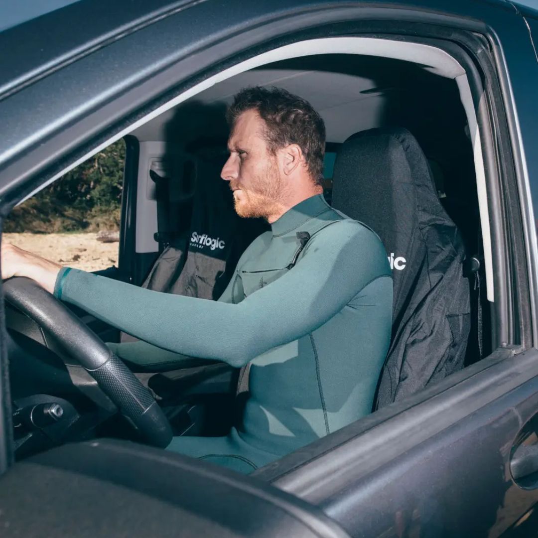 Un surfista con traje de neopreno puesto conduce sentado sobre la Funda de Asiento de Coche Surflogic Black