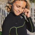 Niño surfista con traje de neopreno colocándose los tapones oídos surf SurfEars Junior 2.0 red teal con codificación por color izquierdo teal y derecho rojo.