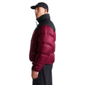 Perfil del modelo con la chaqueta de plumas The North Face Nuptse granate, de cuello alto negro, mangas acolchadas y número 700 en el puño, con gorra y pantalón negro.