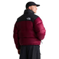 Espalda de la chaqueta de plumas The North Face Nuptse en granate con canesú negro y logo bordado, cuello alto y gorra negra; el modelo mira hacia un lado.