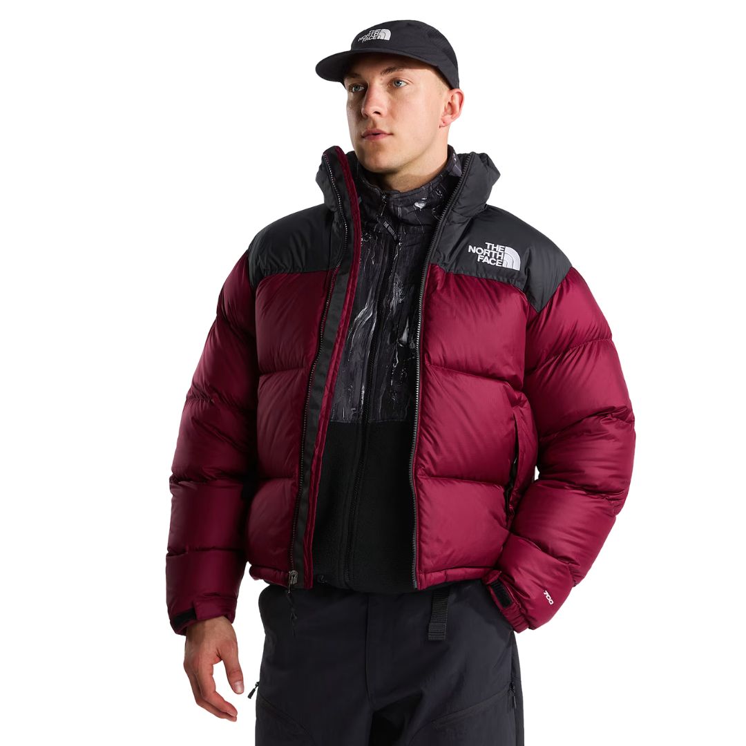 Modelo con la chaqueta de plumas The North Face Nuptse granate y hombros negros, abierta sobre un forro polar estampado, con gorra negra y pantalón técnico oscuro.