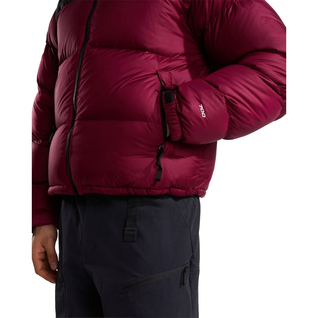 Lateral de la chaqueta de plumas The North Face Nuptse granate con la mano en el bolsillo con cremallera, costuras acolchadas horizontales y la etiqueta 700 en la manga.