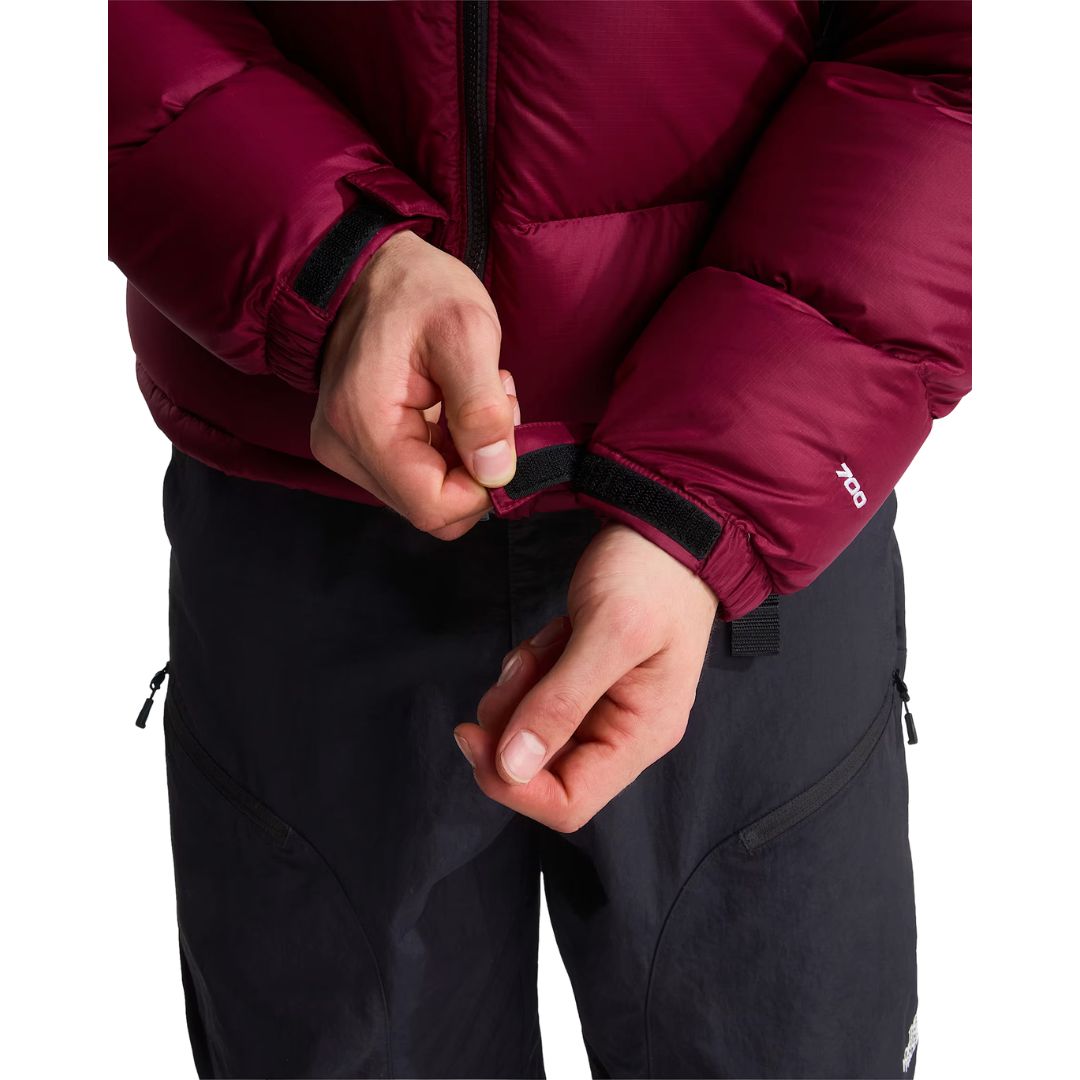 Modelo ajustando el puño con cierre de velcro de la chaqueta de plumas The North Face Nuptse en granate; en la manga se ve el número 700 que indica el relleno de plumón.