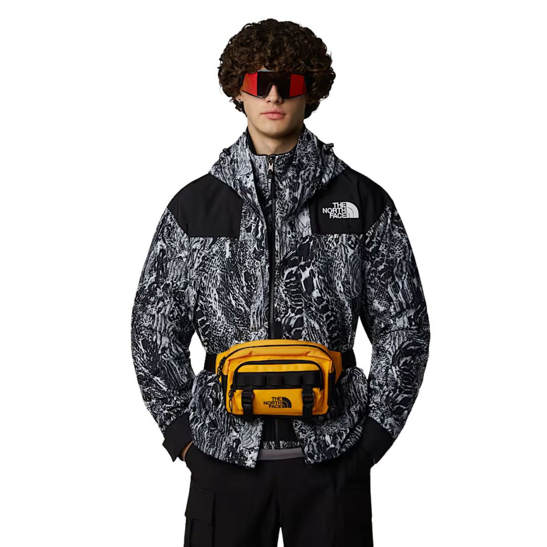 Riñonera The North Face Base Camp Lumbar Summit Gold TNF Black en uso sobre chaqueta con estampado gráfico