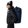 Persona de pie llevando la bolsa The North Face Base Camp Voyager Duffel 42L en color Shady Blue Summit Navy como mochila.