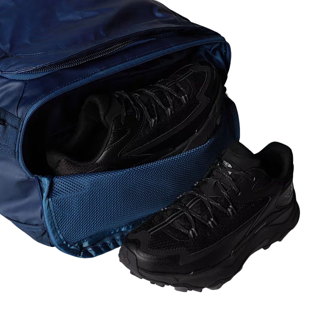 Detalle del compartimento lateral con cremallera de la bolsa The North Face Base Camp Voyager Duffel 42L en color Shady Blue Summit Navy con calzado en el interior.