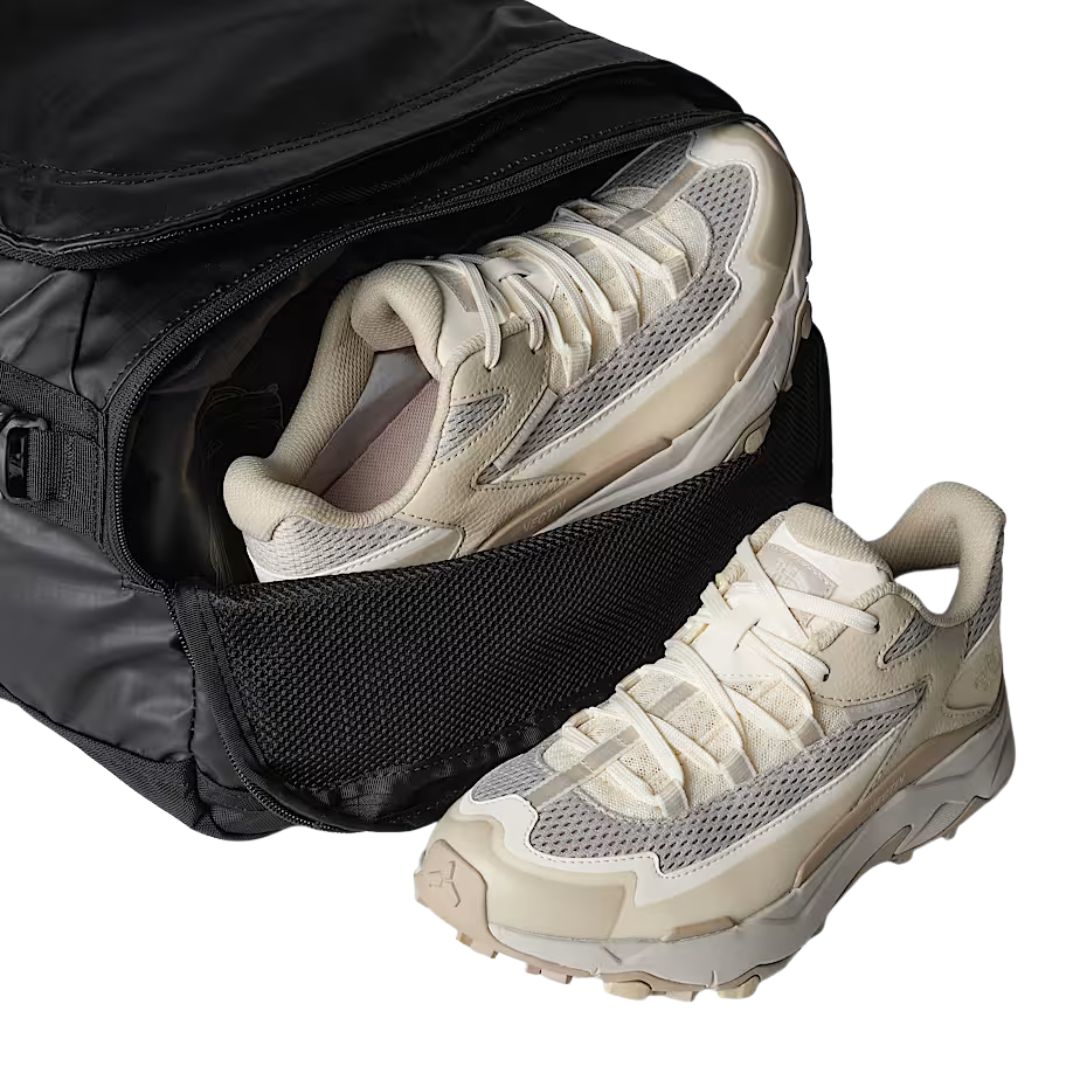 Detalle del compartimento lateral con cremallera de la bolsa The North Face Base Camp Voyager Duffel 42L en color TFN Black Asphalt Grey con calzado en el interior.