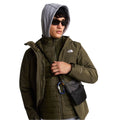 Modelo con la chaqueta The North Face Carto Mono Triclimate en New Taupe Green abierta y bandolera cruzada, dejando ver la capa interior acolchada y el logotipo en el pecho.