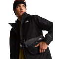 Modelo mirando de lado con la chaqueta The North Face Carto Mono Triclimate negra, bolso bandolera con mosquetón, gafas sobre el gorro y rotulado DRYVENT-MONO en la manga.