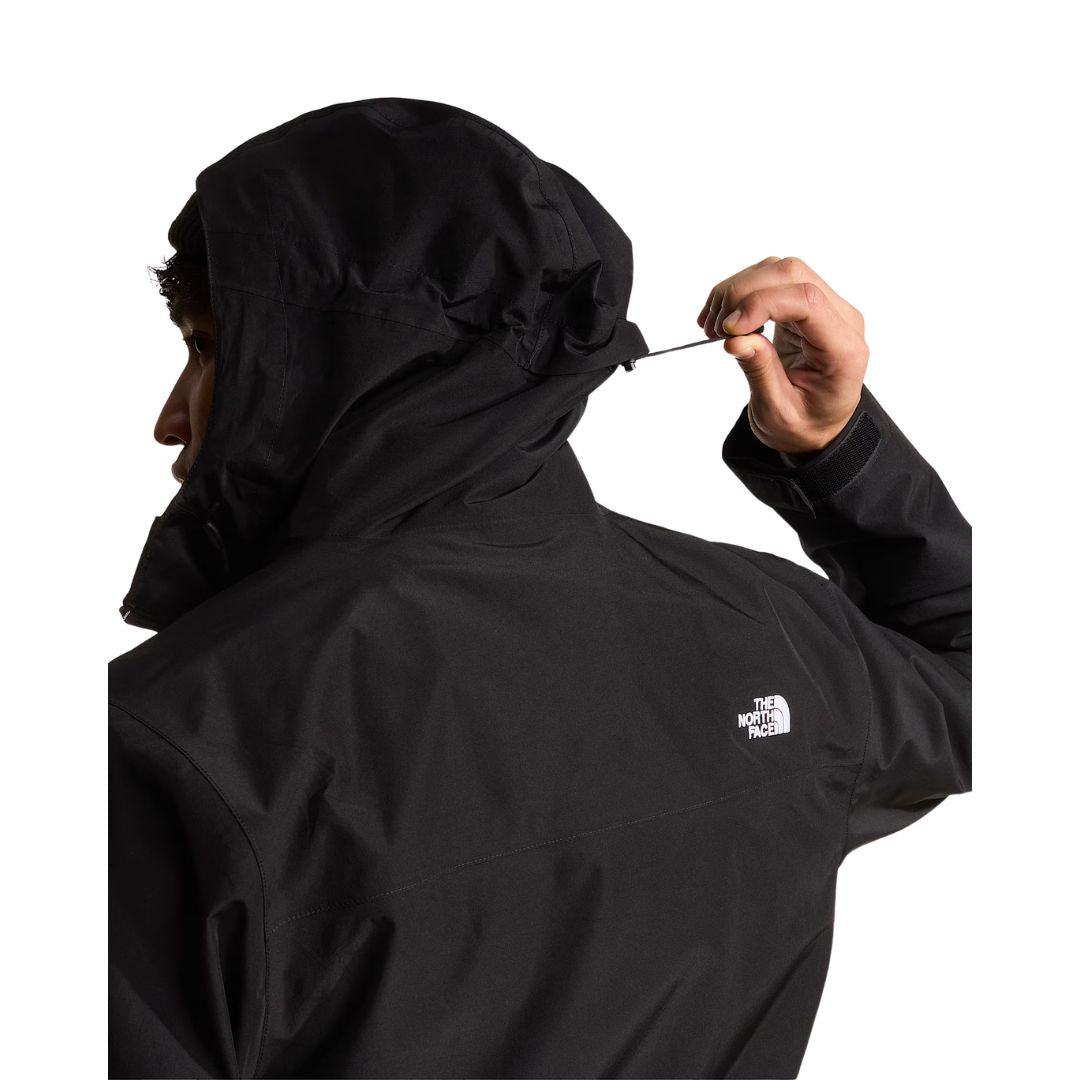 Modelo de espaldas ajustando el cordón de la capucha de la chaqueta The North Face Carto Mono Triclimate negra, con el logotipo bordado en la espalda y el puño con velcro.