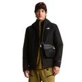 Hombre con la chaqueta The North Face Carto Mono Triclimate negra abierta, bolso bandolera con mosquetón y gafas sobre el gorro, con el logo The North Face bordado en el pecho.
