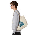 Bolso tote The North Face Cotton Tote con estampado gráfico en lateral, color natural con logo azul, mostrado en modelo lateral