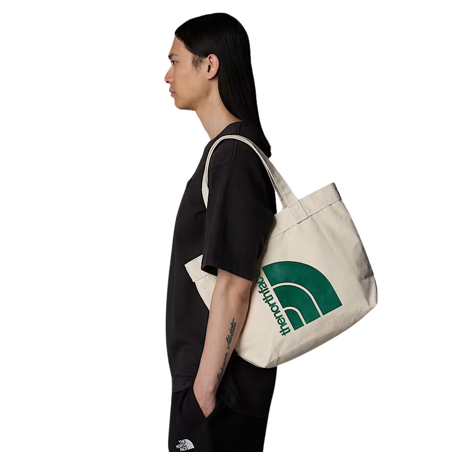 Mujer llevando el bolso The North Face Cotton Tote con diseño "Never Stop Exploring" en el hombro.