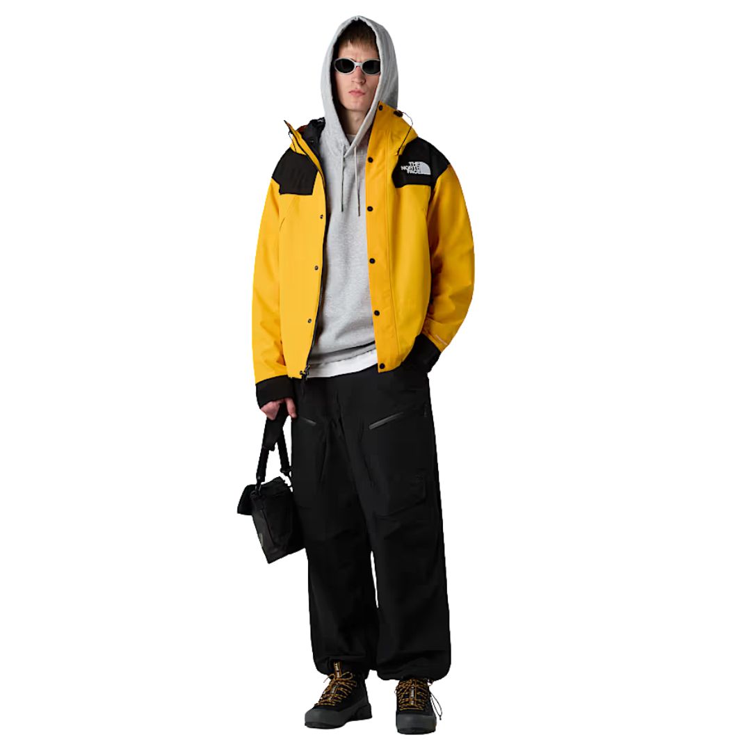 Look completo con chaqueta The North Face Dryvent Mono Mountain Summit Gold y negro TNF, combinada con pantalones negros y sudadera gris.