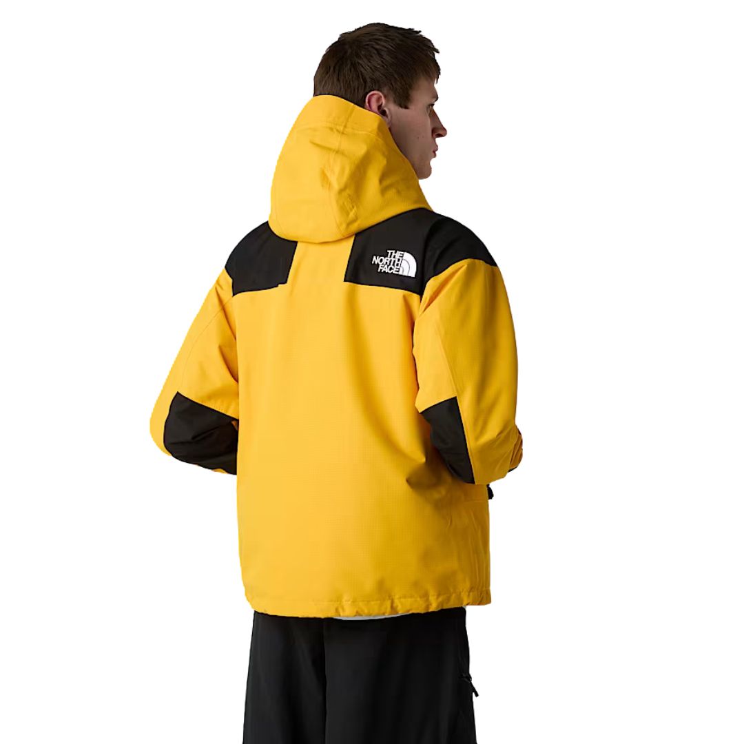 Modelo con chaqueta The North Face Dryvent Mono Mountain Summit Gold y negro TNF, vista trasera.