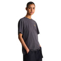 Camiseta The North Face Gear Up Get Out RLX en gris antracita puesta en modelo mujer, vista de perfil mostrando el gráfico pequeño del mochilero con logo amarillo/mostaza en el pecho.