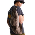 Camiseta The North Face Gear Up Get Out RLX en gris antracita puesta en modelo hombre con sombrero de pescador y gafas de sol, luciendo bandolera color topo cruzada al hombro sobre el gráfico trasero.
