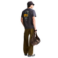 Camiseta The North Face Gear Up Get Out RLX en gris antracita puesta en modelo hombre, vista de espalda mostrando el gráfico completo del mochilero cargado con mochila amarilla, cuerdas y piolets, y sombrero de pescador a juego.