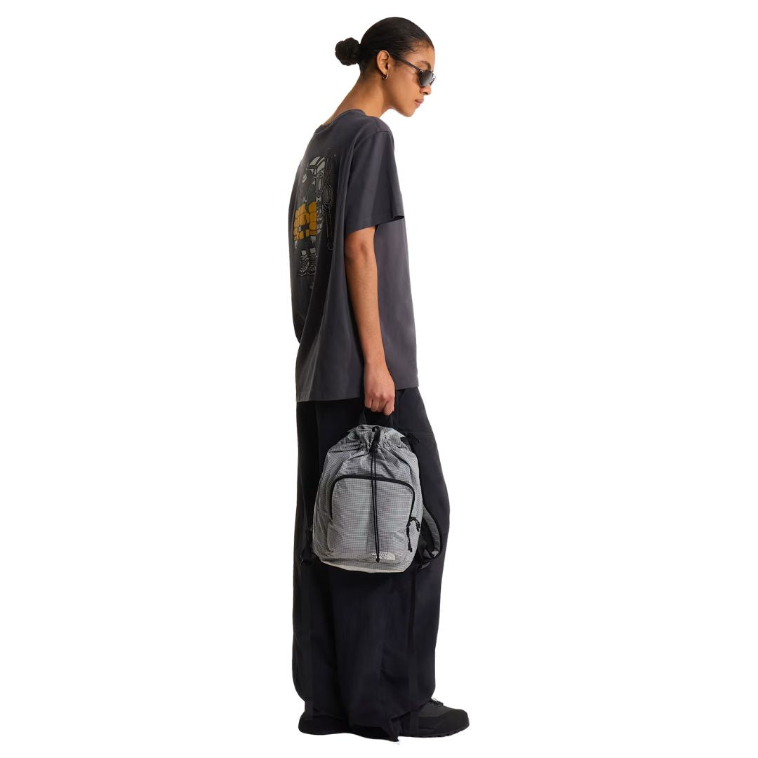 Camiseta The North Face Gear Up Get Out RLX en gris antracita puesta en modelo mujer, vista lateral de perfil con mochila gris a cuadros en la mano y gafas de sol, luciendo el gráfico trasero.