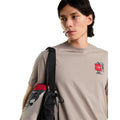 Camiseta The North Face Gear Up Get Out RLX en color piedra puesta en modelo hombre, primer plano del gráfico pequeño del mochilero con logo rojo en el pecho, con bandolera negra cruzada al hombro.