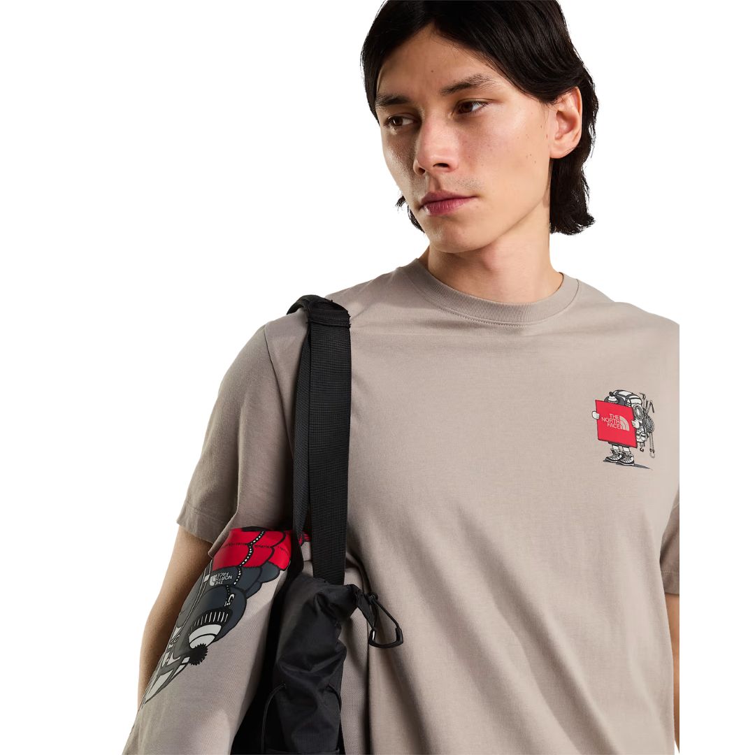 Camiseta The North Face Gear Up Get Out RLX en color piedra puesta en modelo hombre, primer plano del gráfico pequeño del mochilero con logo rojo en el pecho, con bandolera negra cruzada al hombro.