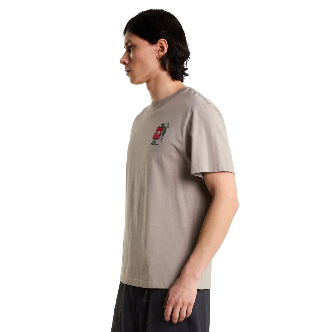 Camiseta The North Face Gear Up Get Out RLX en color piedra puesta en modelo hombre, vista lateral de perfil mostrando el gráfico pequeño del mochilero con logo rojo en el pecho.