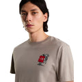 Camiseta The North Face Gear Up Get Out RLX en color piedra puesta en modelo hombre, primer plano del cuello y el gráfico pequeño del mochilero con logo rojo en el pecho.