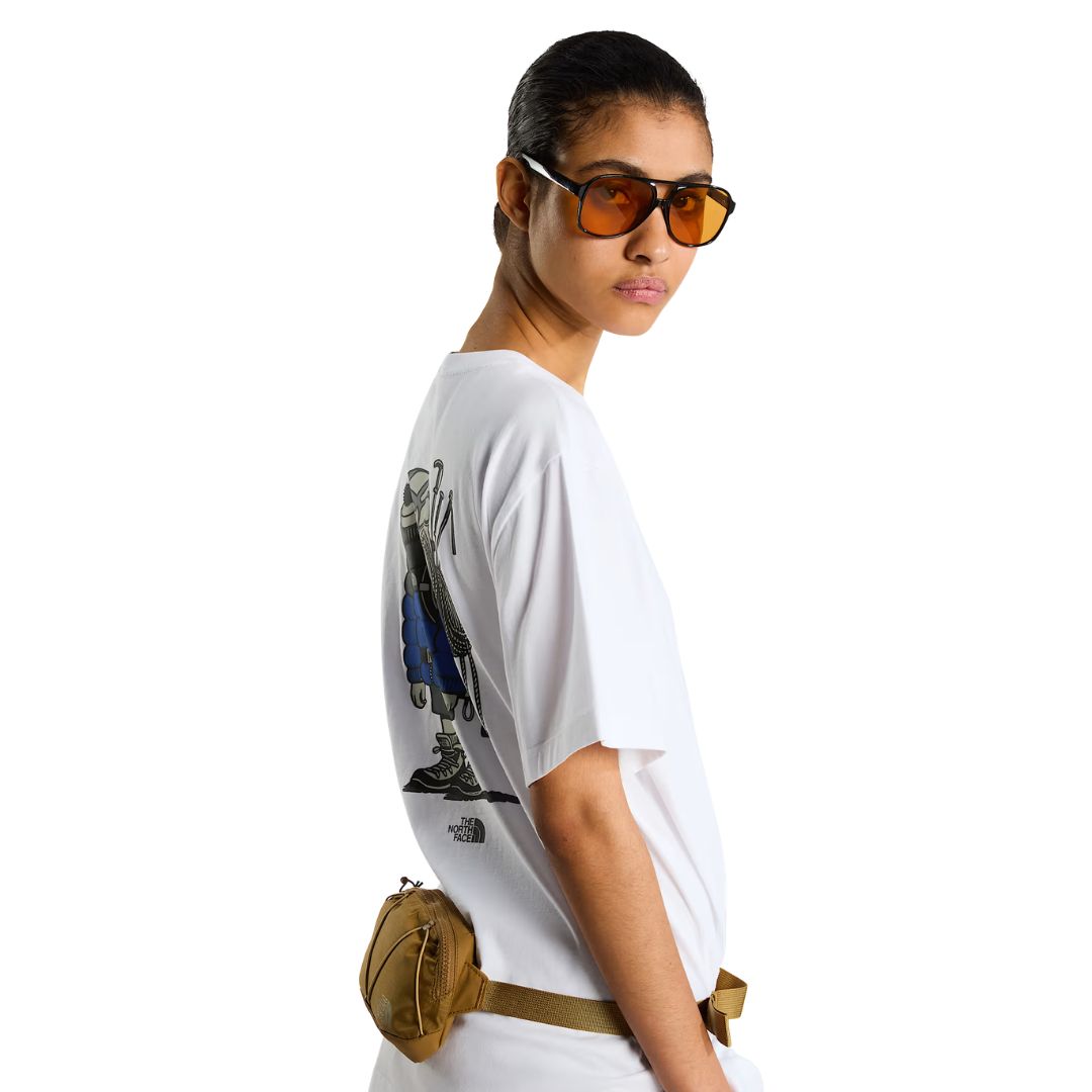 Camiseta The North Face Gear Up Get Out RLX en blanco puesta en modelo mujer, vista lateral de perfil con gafas de sol y riñonera mostaza de la marca a la cintura, luciendo el gráfico trasero.