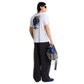 Camiseta The North Face Gear Up Get Out RLX en blanco en modelo hombre de cuerpo entero por detrás, combinada con pantalón ancho negro y mochila gris a juego en la mano, luciendo el gráfico trasero.
