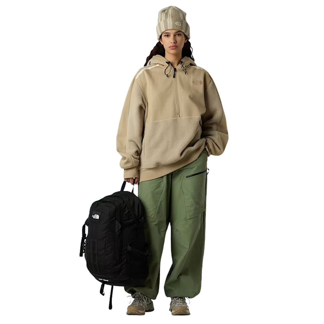 Mujer con sudadera beige y pantalón verde sosteniendo la mochila The North Face Hot Shot SE en color negro.