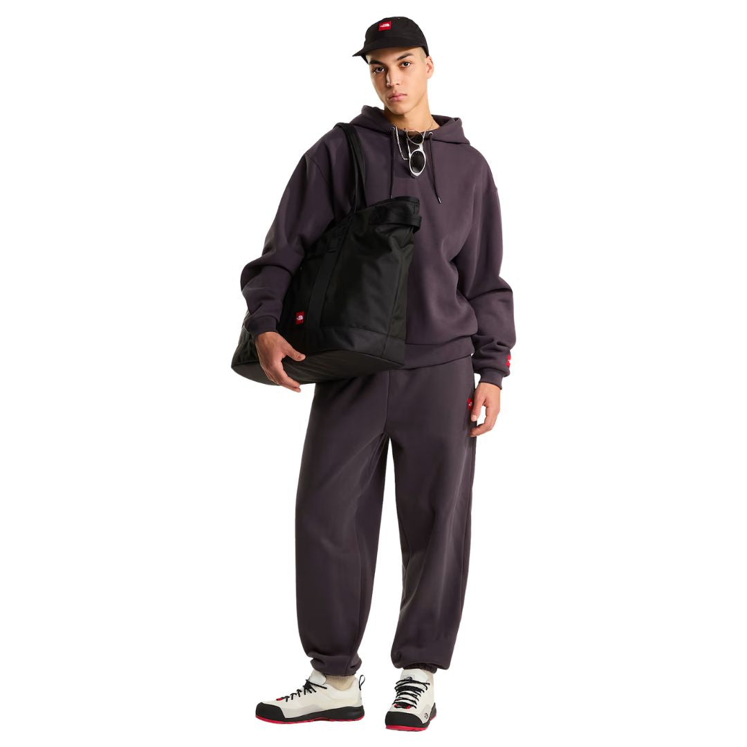 Look completo en modelo con el pantalón de chándal Red Box de The North Face en color Obsidian, combinado con sudadera con capucha, gorra y bolso tote de la marca.