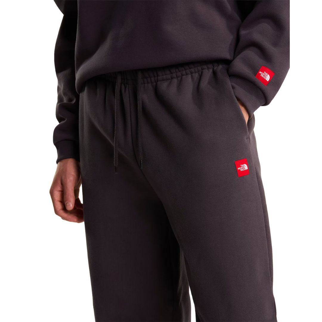 Detalle de la cintura elástica con cordón ajustable del pantalón de chándal Red Box de The North Face en color Obsidian, junto al parche bordado Red Box del bolsillo lateral.