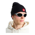 Modelo con gafas de sol y sudadera clara lleva el gorro The North Face Red Box Beanie TNF Black, vista frontal con el borde vuelto y el parche rojo con el logo en el puño